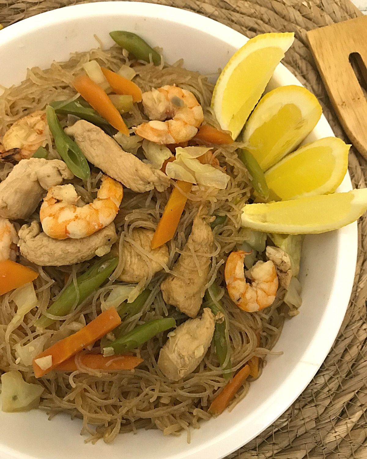 pancit bihon served in a white round plate with lemon slices